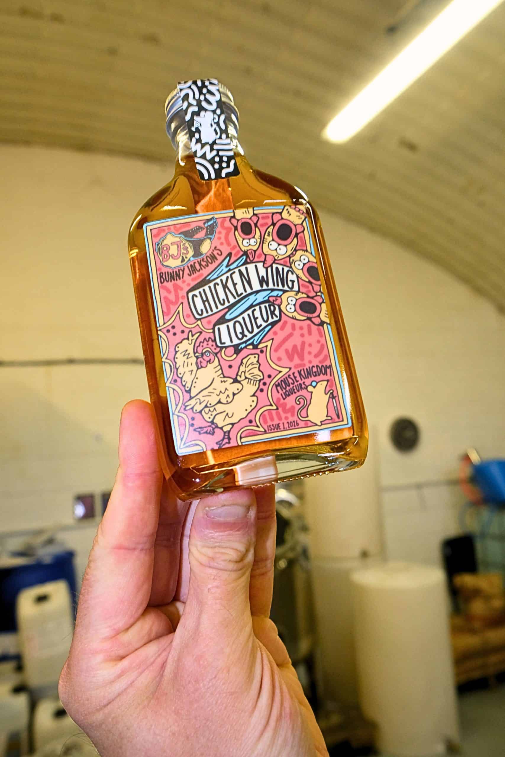 Hand holding a colourful chicken wing liqueur bottle in a room.